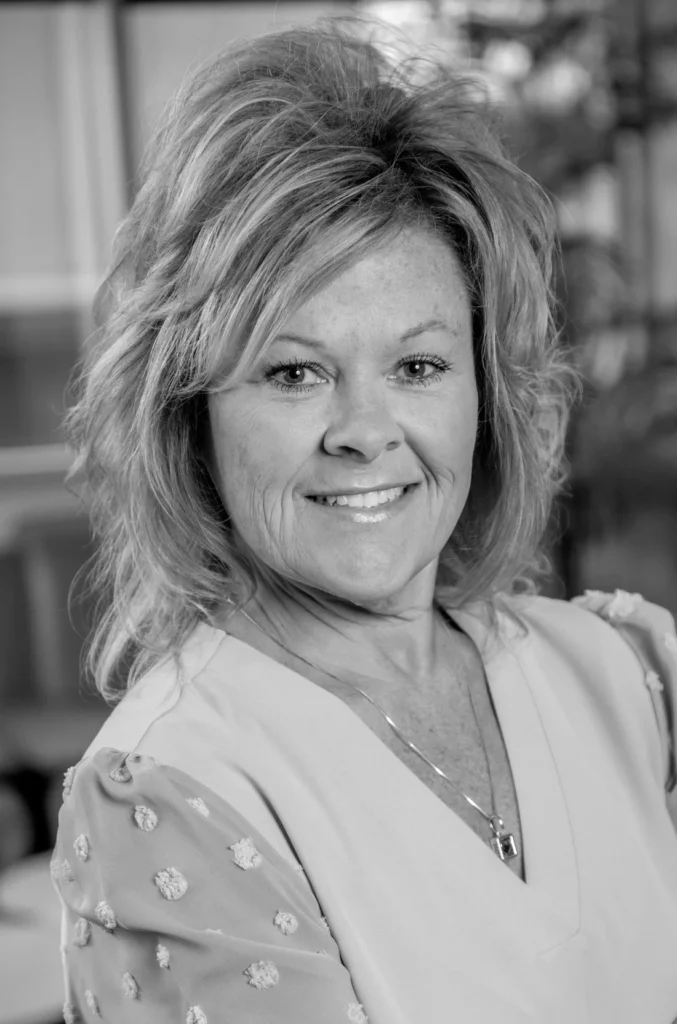 Black and white headshot of a smiling woman with shoulder-length blonde hair