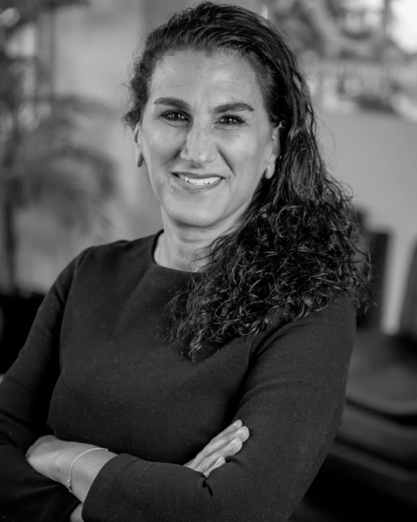 Black-and-white headshot of a smiling woman with curly hair, arms crossed