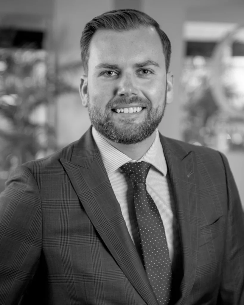Black-and-white headshot of a smiling bearded man in a suit and patterned tie