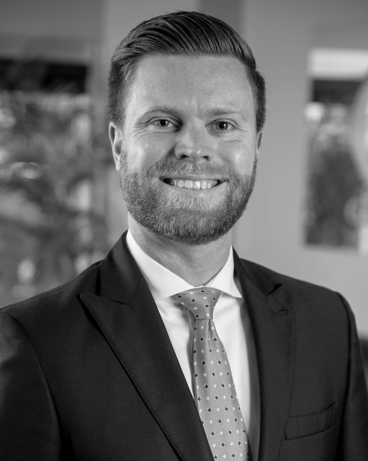 Black-and-white headshot of a smiling bearded man in a suit and tie