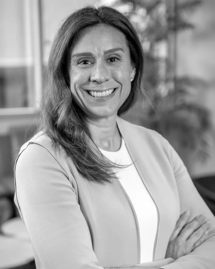 Black-and-white portrait of a smiling woman with long hair, arms crossed, wearing a light cardigan over a white top
