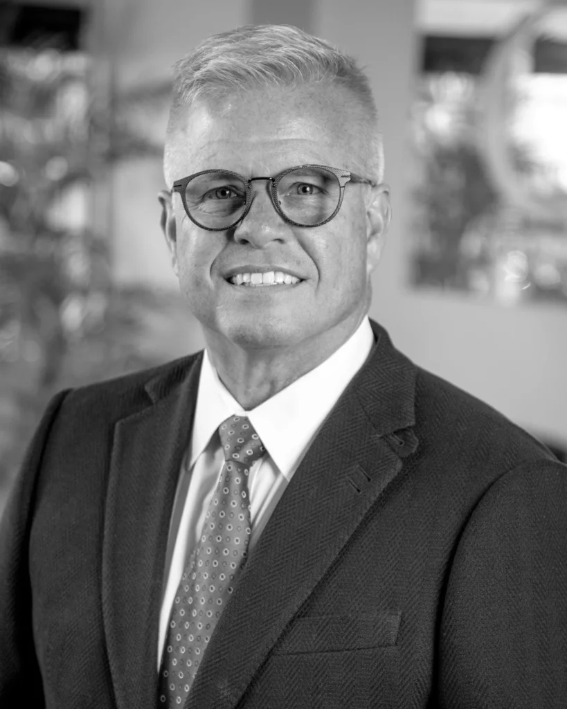 Smiling man in glasses, dark suit and patterned tie, black-and-white professional headshot