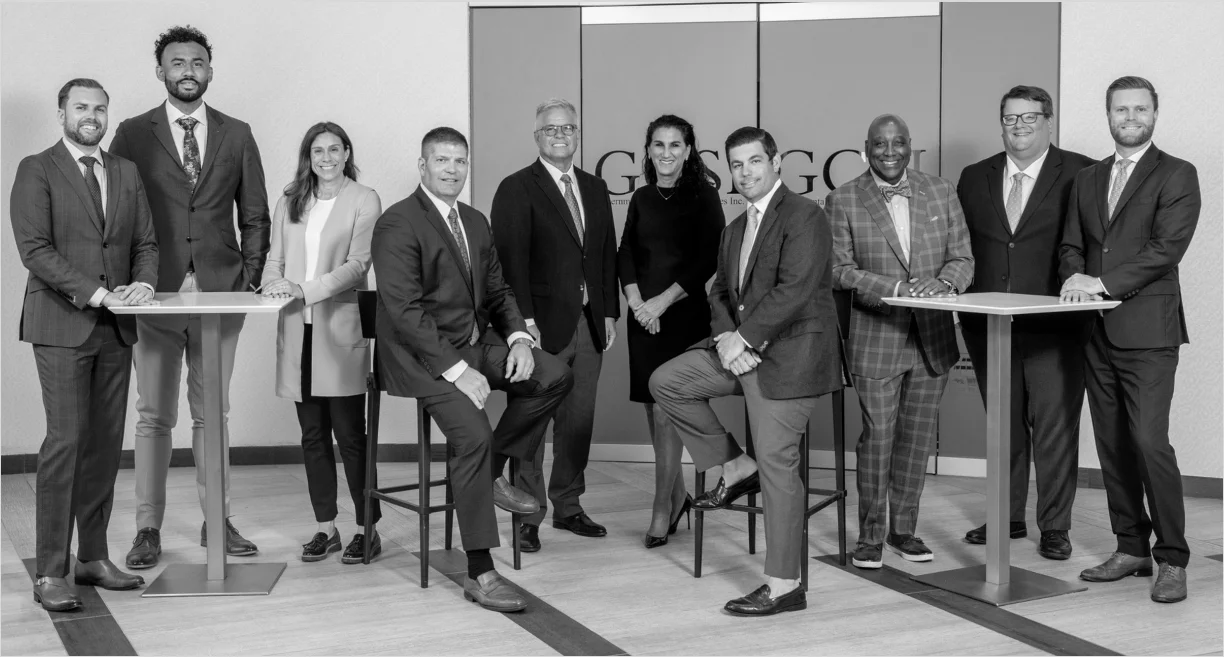 Black-and-white group portrait of ten professionals in business attire posing in an office