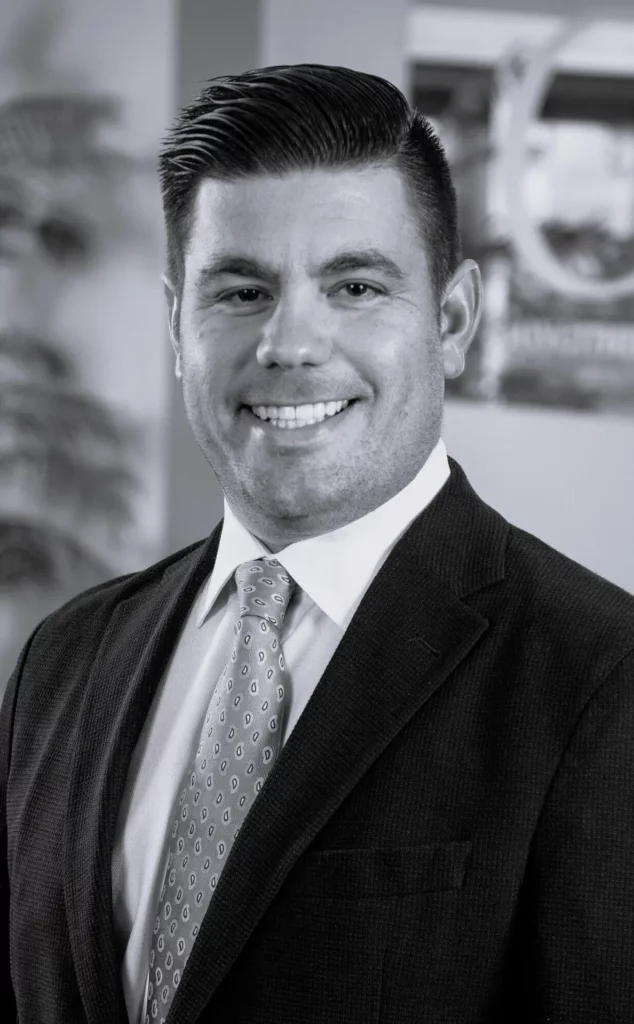 Black-and-white professional headshot of a smiling man in a dark suit and patterned tie